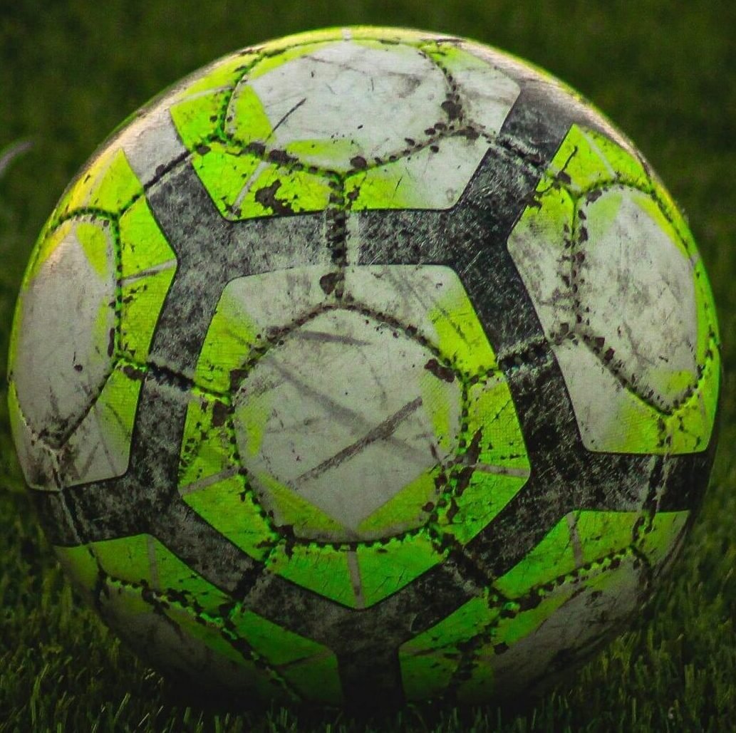 Close-up of a worn soccer ball resting on a green field in Adana, Turkey.